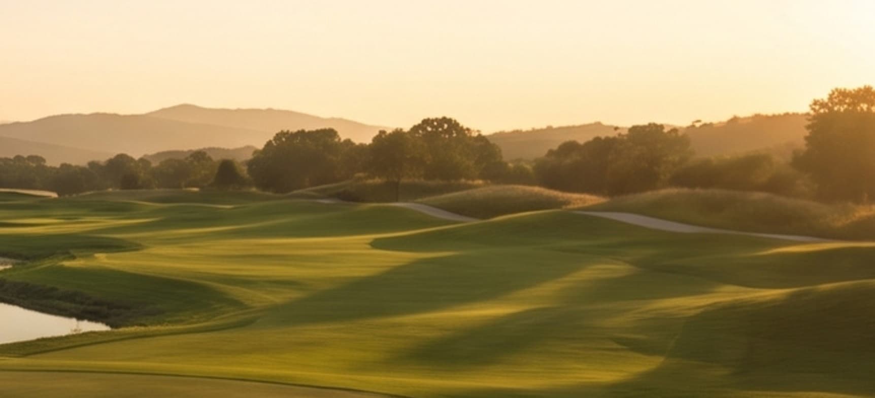 Fairway ondulado com bunkers e montanhas ao fundo, na luz dourada do entardecer